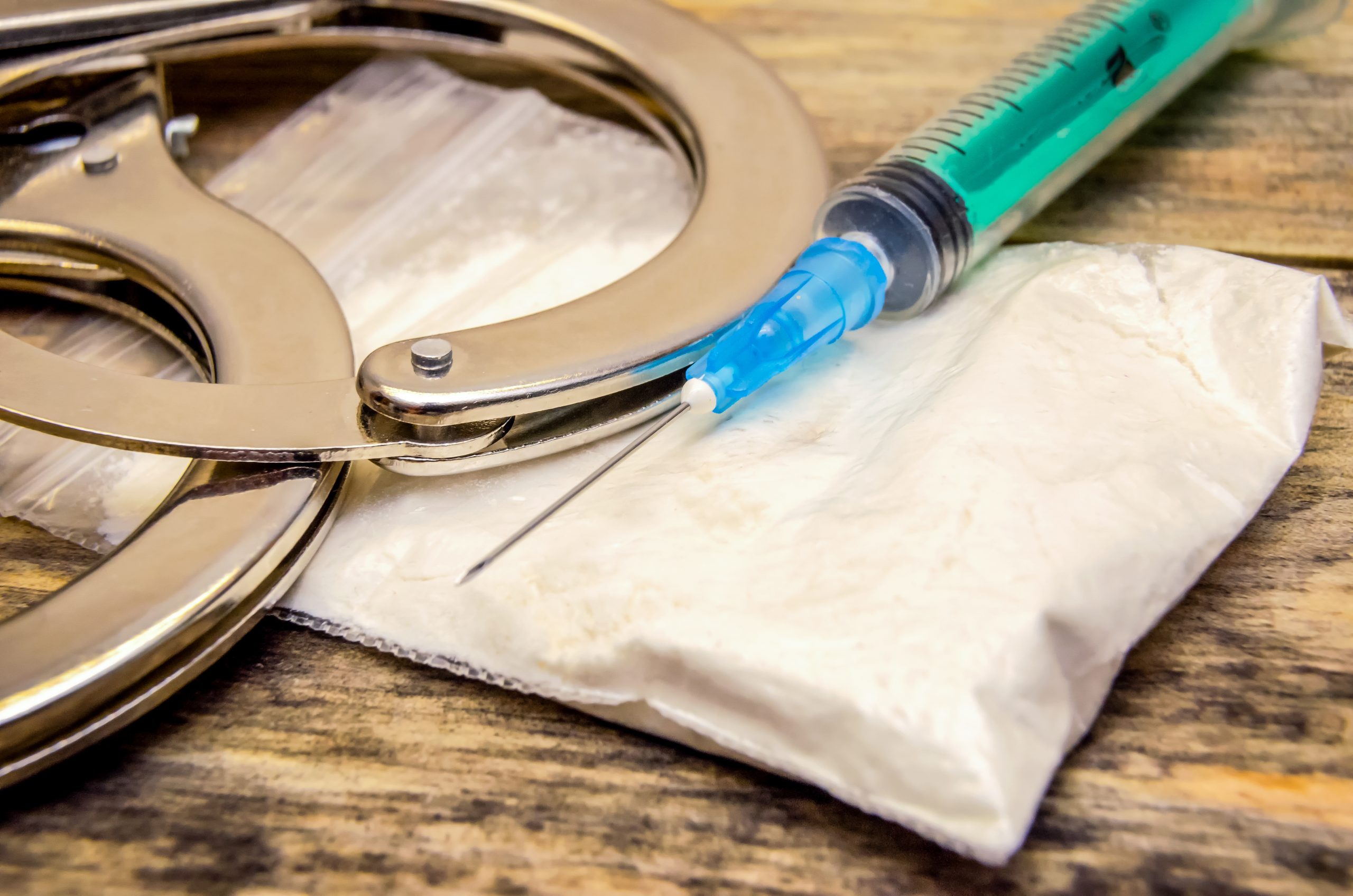 Handcuffs, syringe, bag of drugs on a wooden background close-up